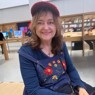 A smiling woman wearing a red cap and floral embroidered blue jacket indoors.