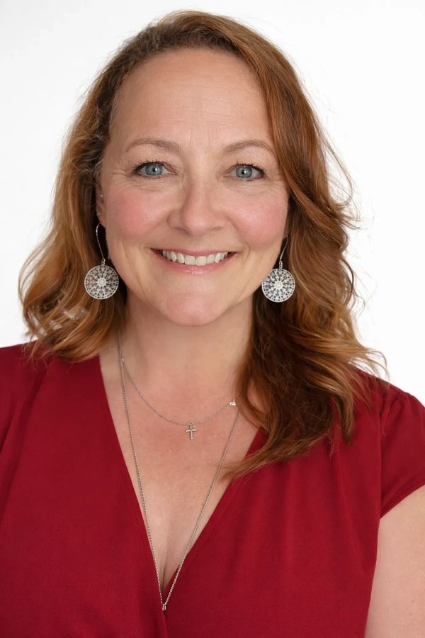 Smiling woman with red hair wearing a red top and silver jewelry.