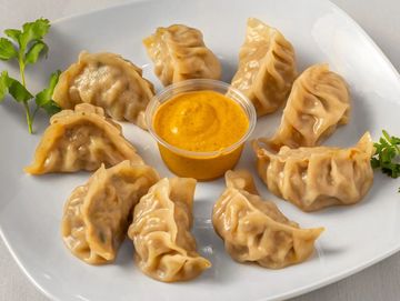 Plate of steamed dumplings with a creamy dipping sauce and garnished with cilantro.