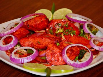 Spicy grilled chicken pieces garnished with onion rings and lime slices on a white plate.