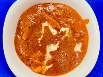 A bowl of creamy butter chicken curry garnished with cream.