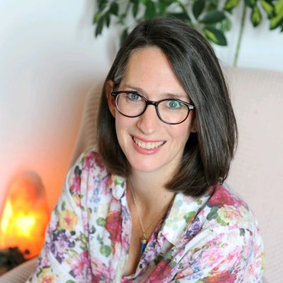 Woman with glasses smiling, wearing a floral shirt.