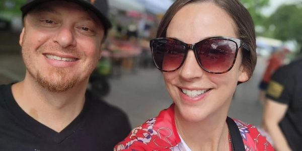 Smiling couple outdoors, woman wearing sunglasses and floral top.
