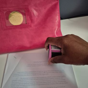 A hand stamping a document with a pink stamp near a pink folder.