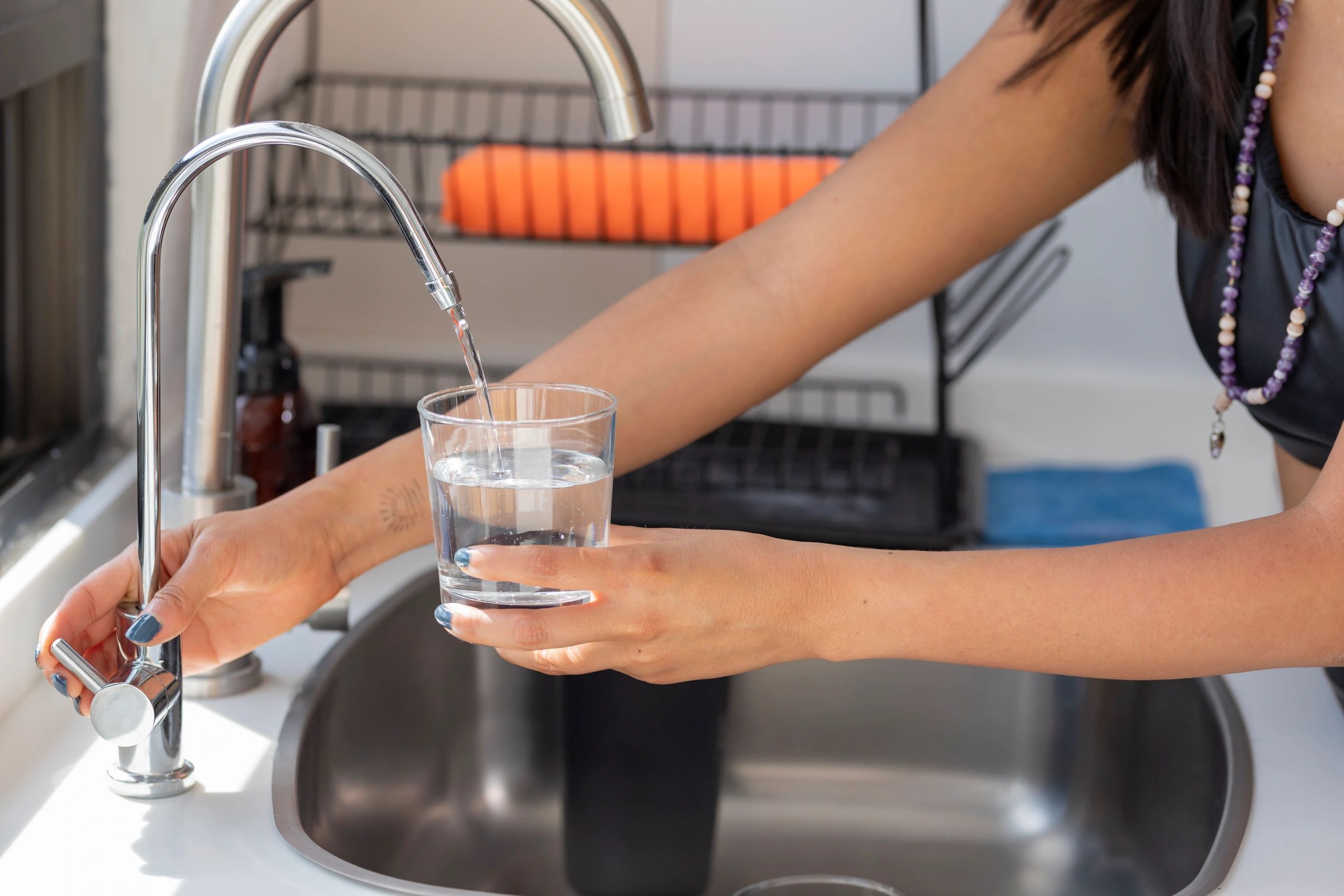 woman's hands filling a water glass at a reverse osmosis filter faucet