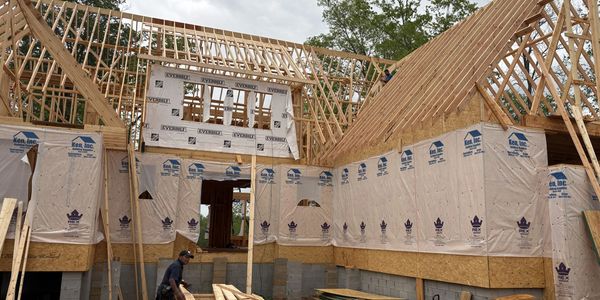 Wooden house frame under construction with workers on site.