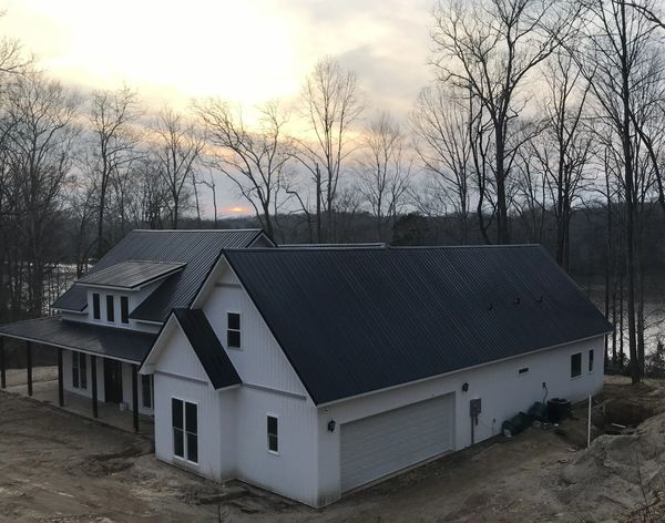 Modern white house with black metal roof at sunset in a wooded area.