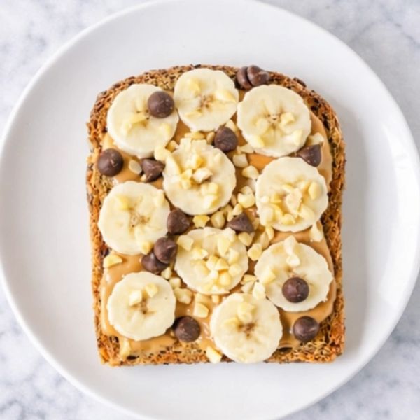 Tostada con crema de maní, banano y chips de chocolate en plato blanco