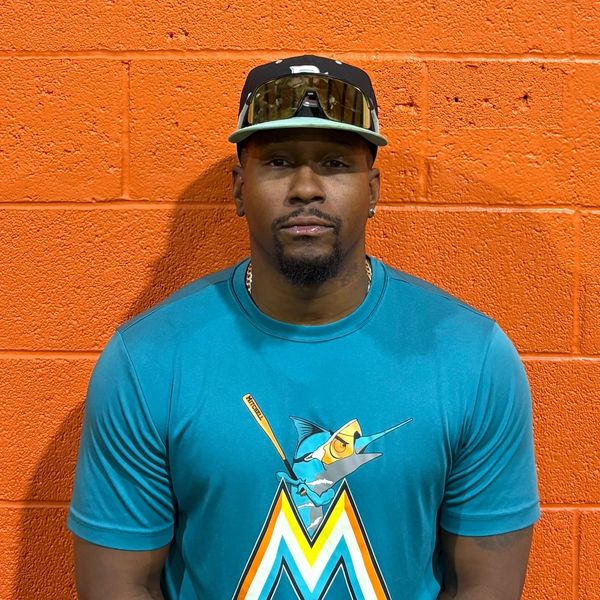 Man wearing a Miami Marlins shirt and black cap against an orange wall.