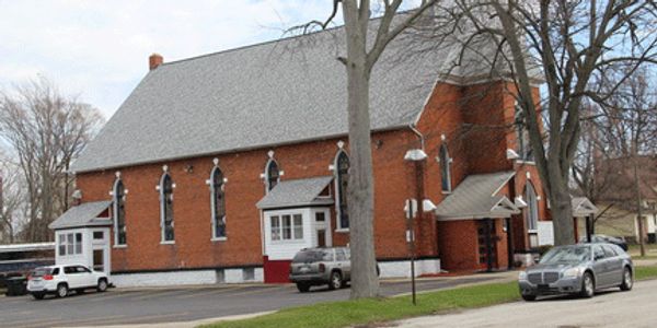 Brick church building with arched windows and parked cars.