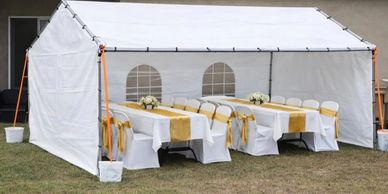 White outdoor tent with decorated tables and chairs for an event.