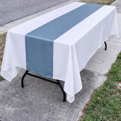 A white tablecloth with a blue runner on a black folding table outdoors.