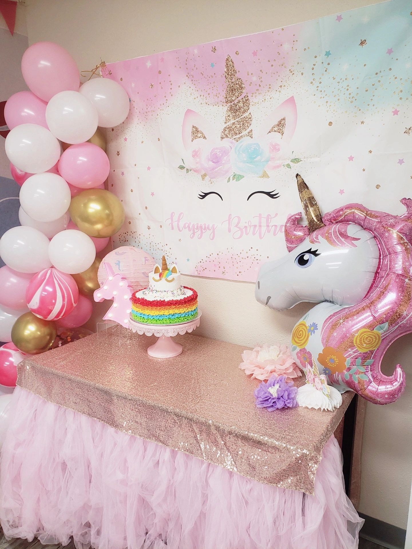 A unicorn birthday setup at Smarty Sprouts with a themed backdrop, pink balloons, cake table and unicorn balloon, showing Flower’s Full Themed Décor.
