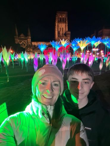 Two people smiling in front of colorful illuminated flowers at night.
