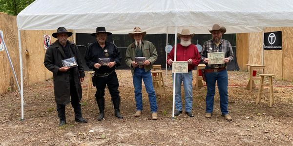 Five men in cowboy attire stand under a white tent holding awards and certificates.