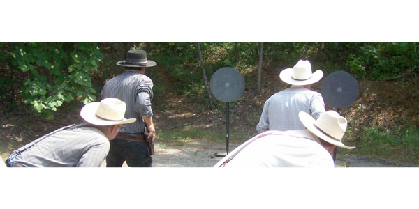 Four men with cowboy hats practicing shooting at metal targets outdoors.