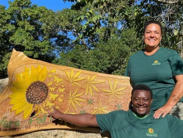 Two people smiling with a carved wooden sign featuring a sunflower and leaves.