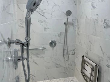 Modern walk-in shower with marble tiles and dual handheld showerheads.