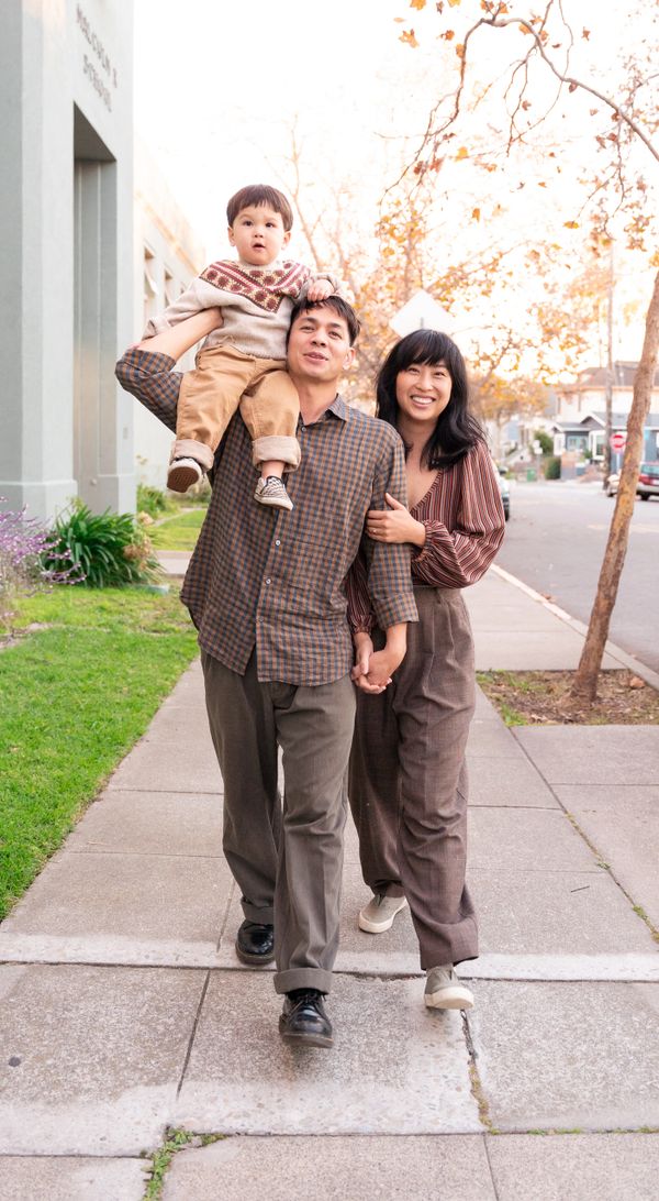 Happy family walking outdoors with child on father's shoulders during autumn.