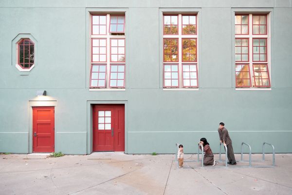 Family with child outside a building with red doors and windows.