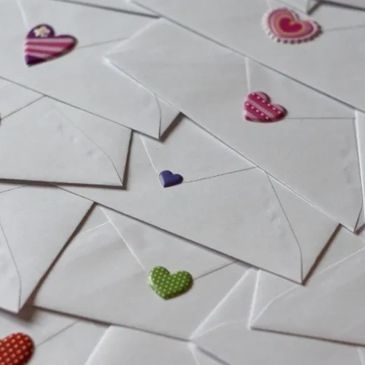 White envelopes sealed with colorful heart stickers scattered on a surface.