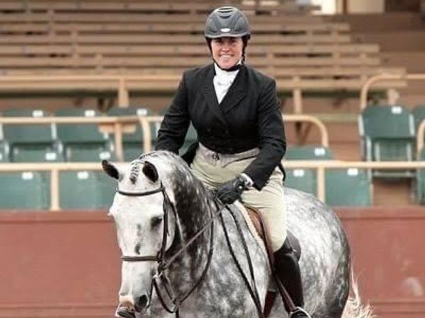 Smiling rider on a dapple gray horse in an arena.