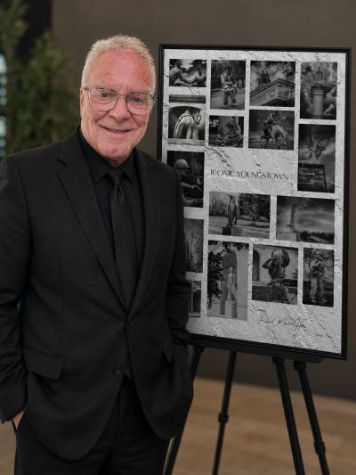Smiling man in black suit stands next to a photo collage on an easel.