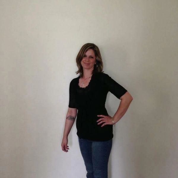 Woman standing against a plain wall, smiling.