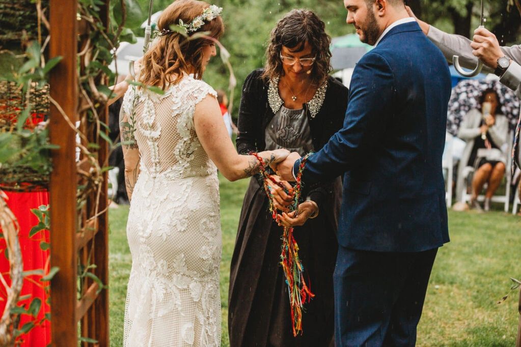 Couple holding hands with officiant during outdoor wedding ceremony.