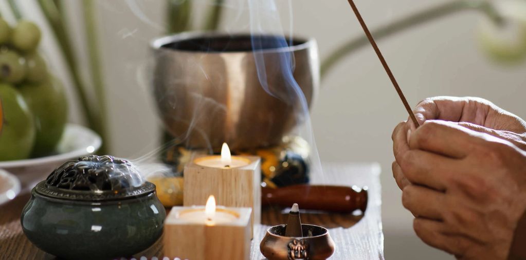 Hands lighting incense sticks near candles and a bowl for a calming atmosphere.