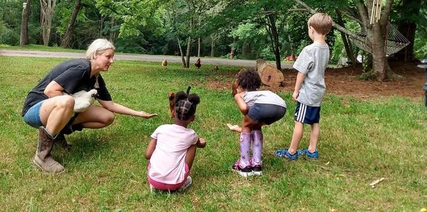 Woman helping children feed chickens at a petting farm
