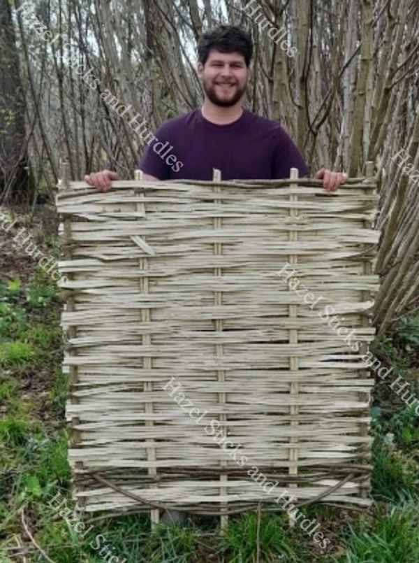 Man holding a woven fence panel outdoors.