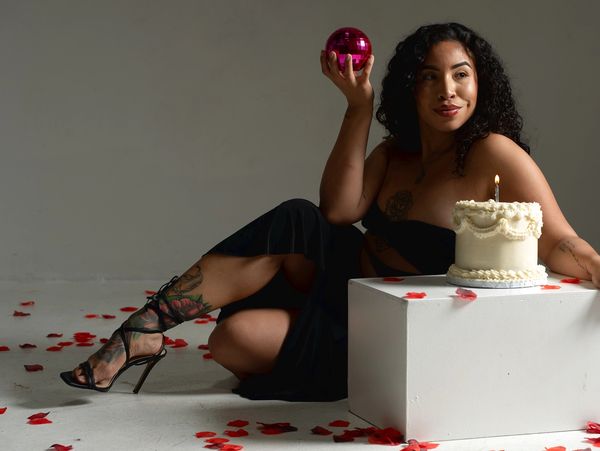 Woman holding pink ornament near a birthday cake on a white block.