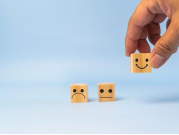 Hand picking a wooden block with a happy face among sad and neutral faces.