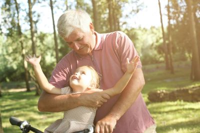 Grandfather joyfully embraces granddaughter outdoors on a sunny day.