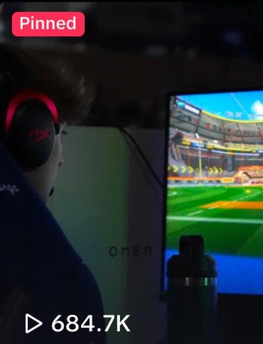 Person gaming with headphones, focused on a soccer video game on a monitor.