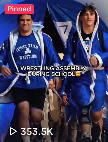 Two wrestlers in blue robes walking confidently during a wrestling assembly at school.