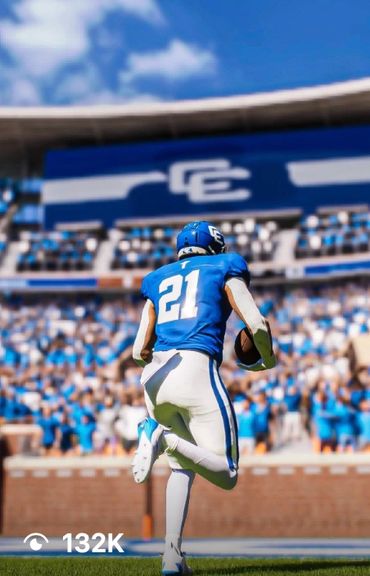 Football player in blue jersey running with ball on field.