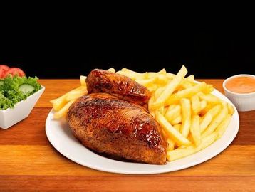 Grilled chicken with French fries and dipping sauce on a wooden table.