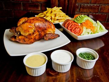 A roasted chicken meal with fries, salad, and three dipping sauces.