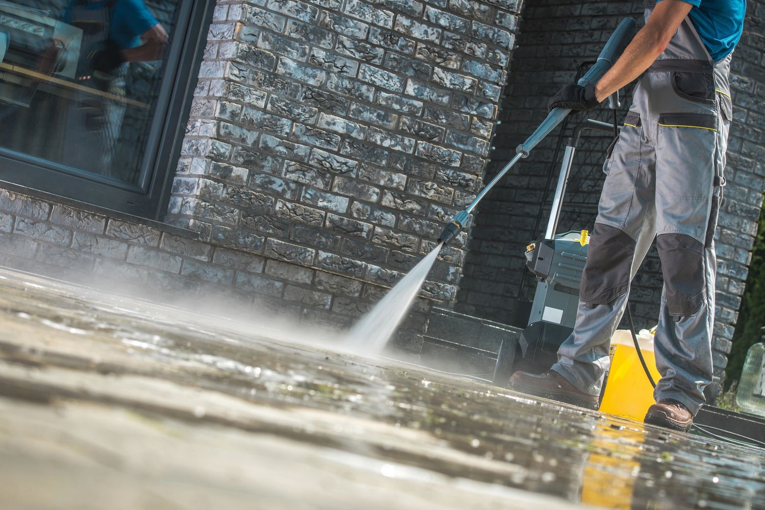 Person pressure washing a stone patio outside a brick house.