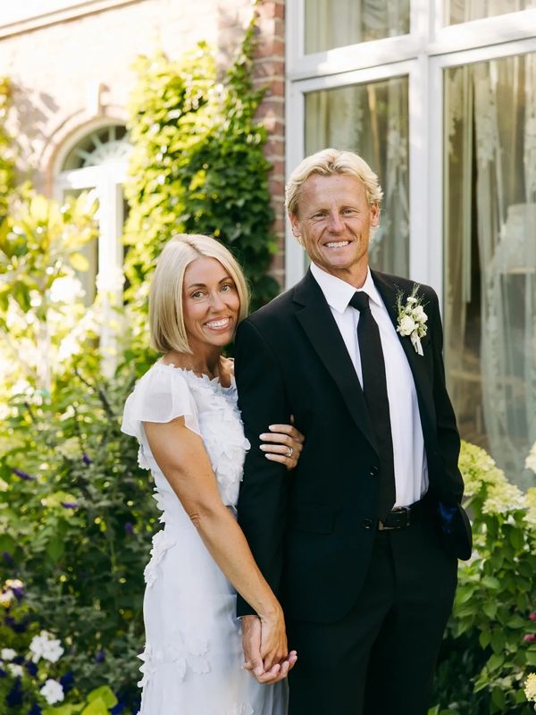 Smiling couple dressed elegantly, holding hands in a garden setting.