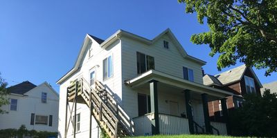 White two-story house with exterior stairs under a clear blue sky.