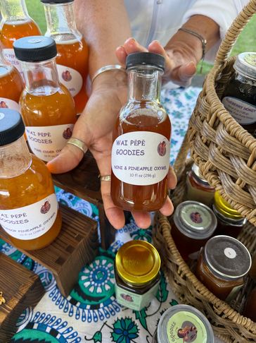 Hand holding a bottle of Wai Pepē Goodies Noni &amp; Pineapple Oxymel among other bottles and jars.
