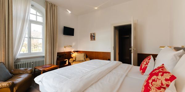Cozy hotel room with white bedding and red decorative pillows.