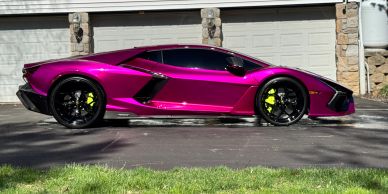 A shiny purple sports car parked in front of a garage.