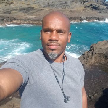Man takes a selfie by the rocky ocean shore on a sunny day.