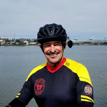 Smiling cyclist in black and yellow jersey by the water with a helmet.