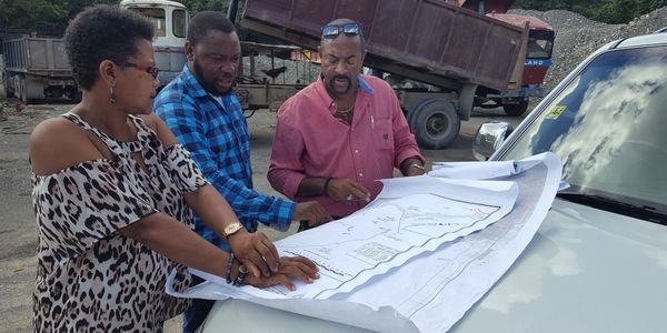 Three people examining a large map on a car hood.