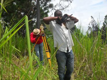 Two men doing land surveying in a grassy field.